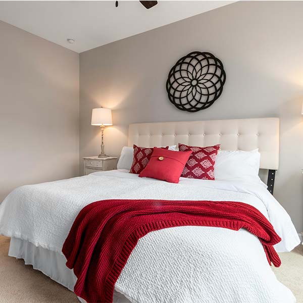 Lit douillet avec linge de lit blanc, jeté de lit rouge tricoté et coussins assortis dans une chambre lumineuse.