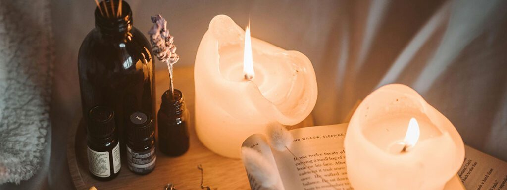 Plateau d'ambiance avec flacons d'huiles essentielles, bougies allumées et un livre ouvert pour une routine de relaxation