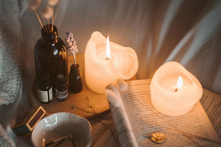 Plateau d'ambiance avec flacons d'huiles essentielles, bougies allumées et un livre ouvert pour une routine de relaxation nocturne