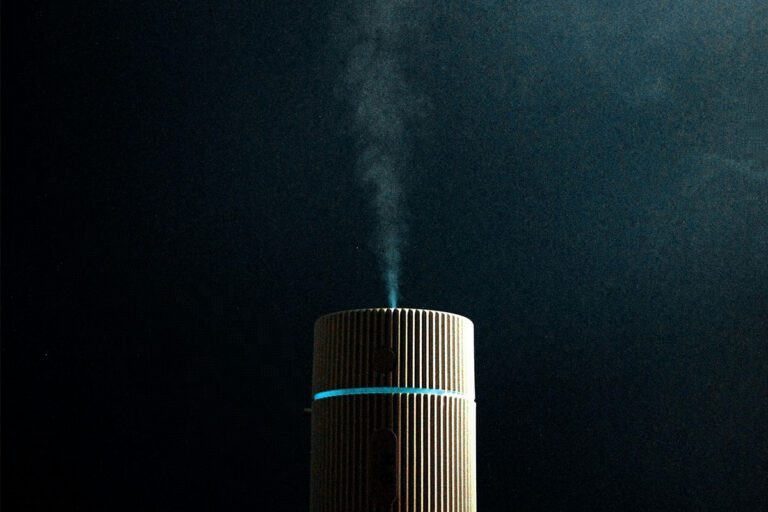 Diffuseur d'huiles essentielles cylindrique effet bois allumé avec brume visible sur fond sombre et éclairage dramatique