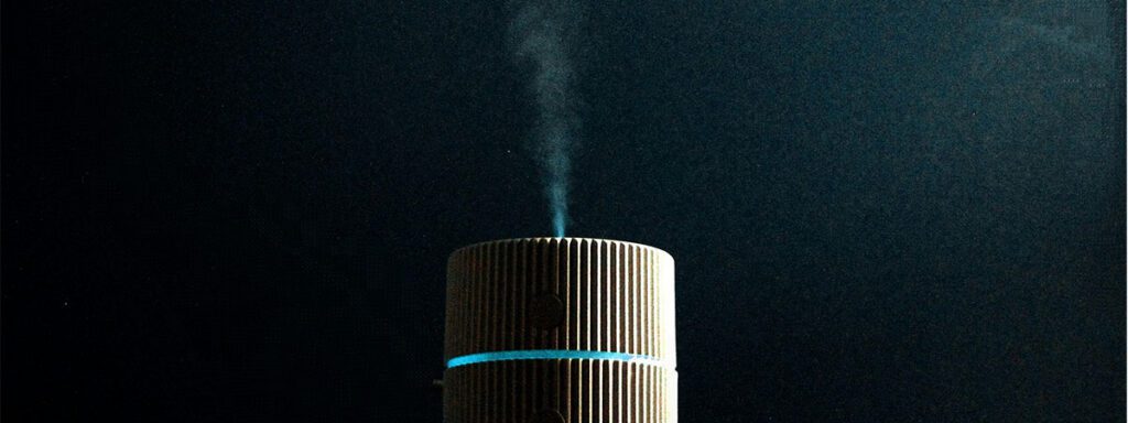 Diffuseur d'huiles essentielles cylindrique allumé avec brume visible sur fond sombre et éclairage dramatique